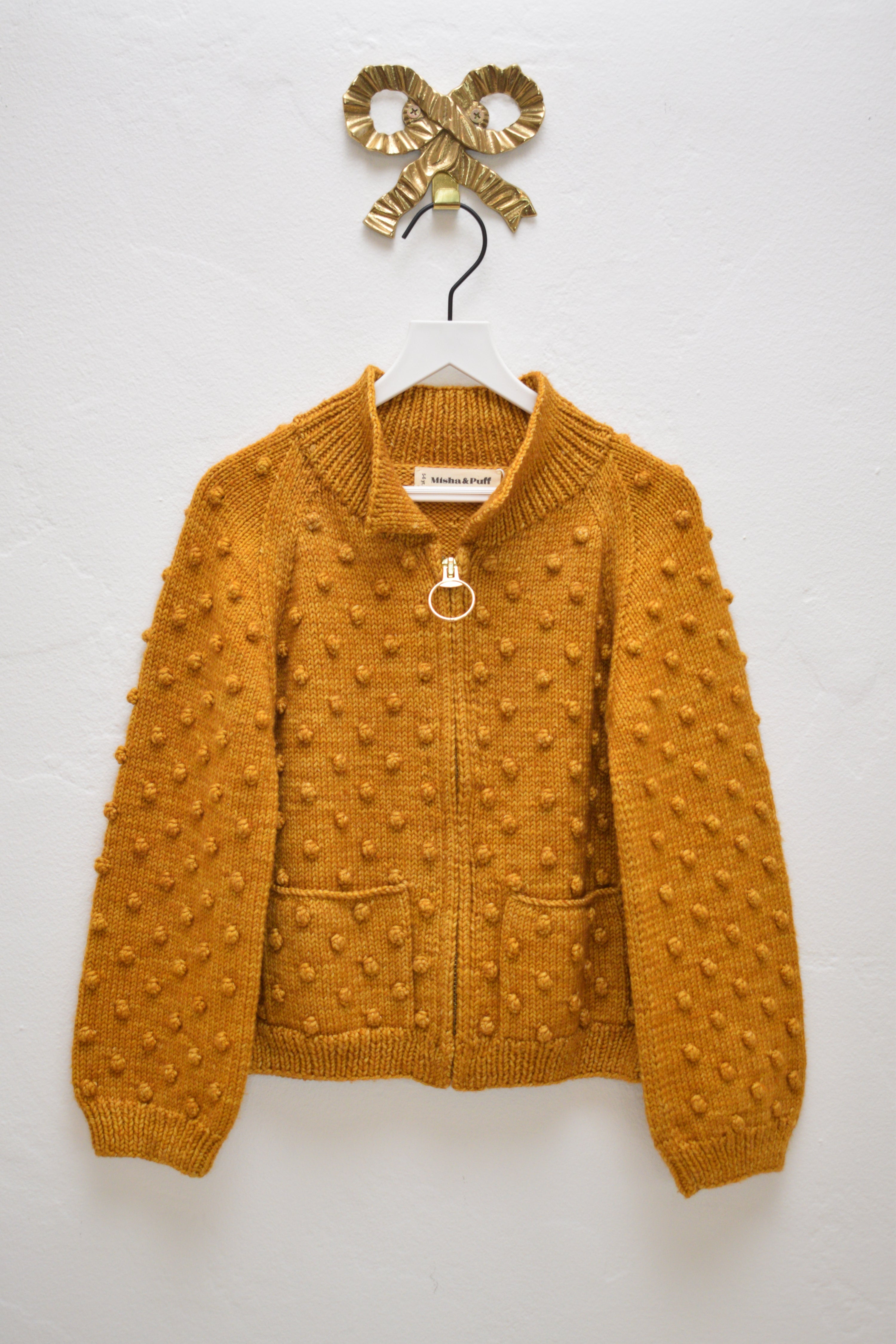 Misha & Puff marigold popcorn zip cardigan with ring pull and patch pockets, size 5–6 years, hanging on a white hanger against a neutral wall