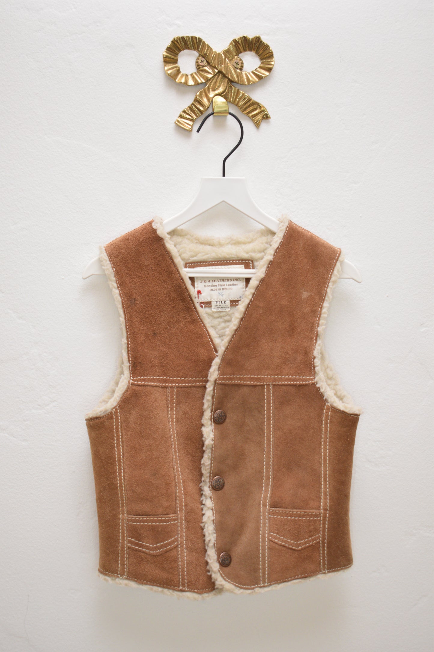 Vintage camel-tan suede kids vest with cream sherpa lining and buttons, size 4–5 years, hanging on a white hanger against a neutral wall.