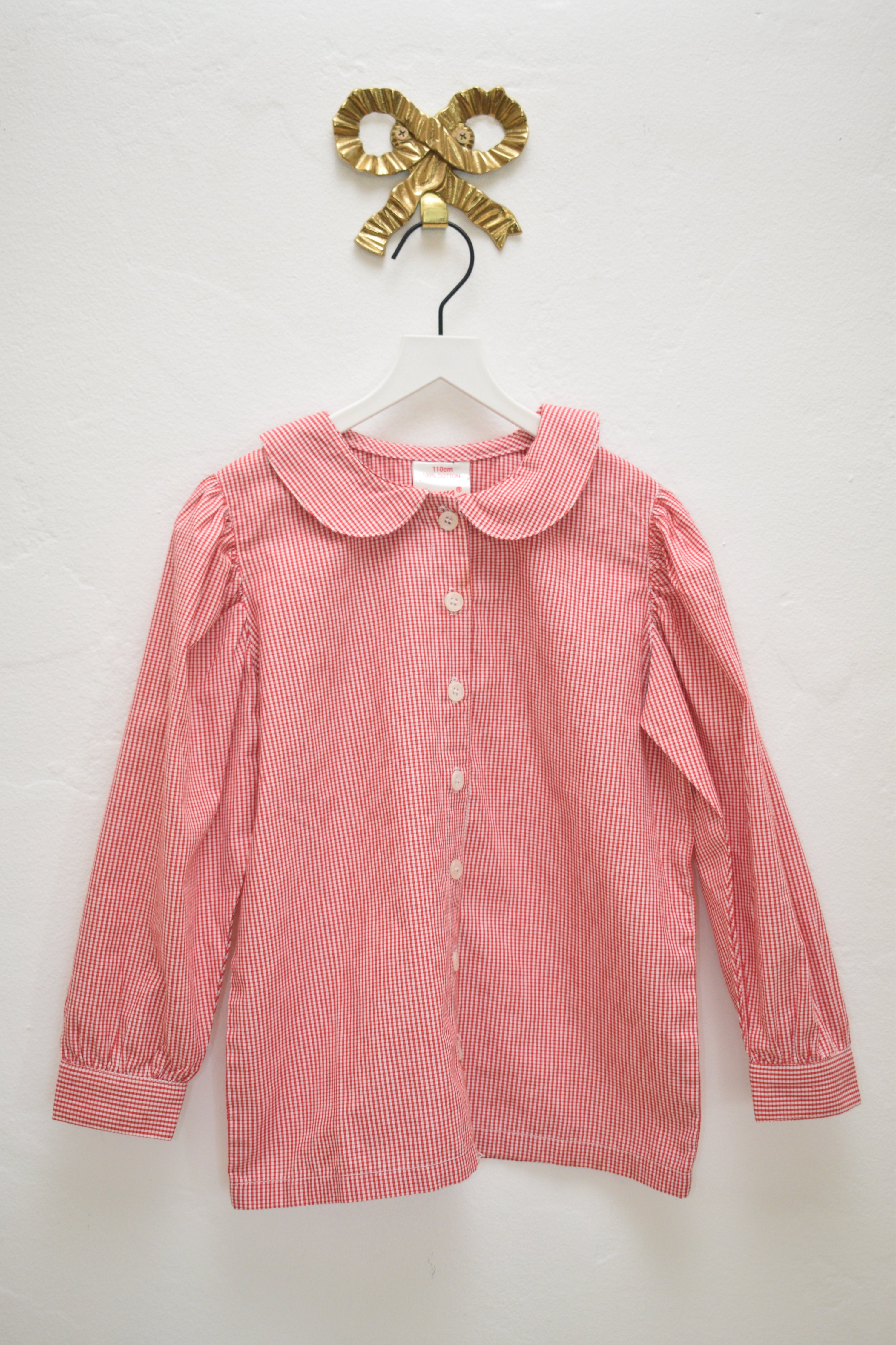 Hanna Andersson red-and-white micro-gingham long-sleeve blouse with Peter Pan collar, size 4–5 years, hanging on a white hanger against a neutral wall.
