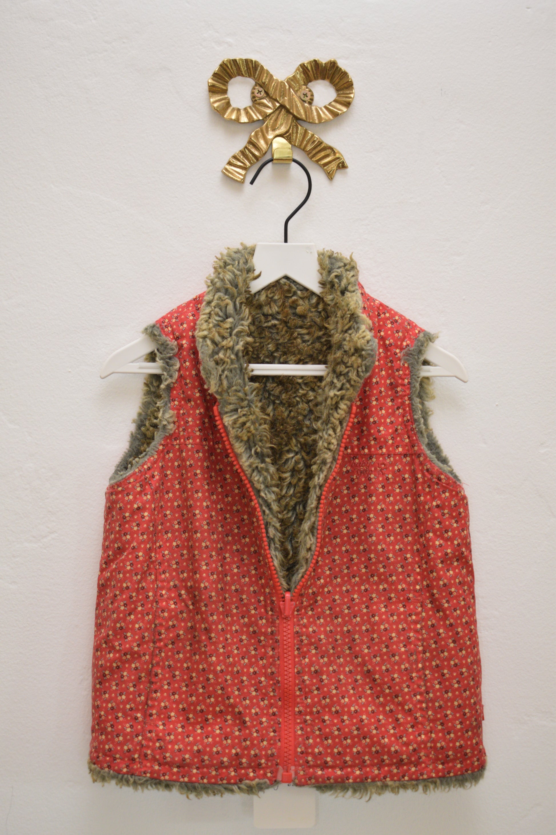 GAP reversible kids vest, olive faux-fur on one side and red floral on the other, zip front, size 2 years, on hanger against neutral wall.