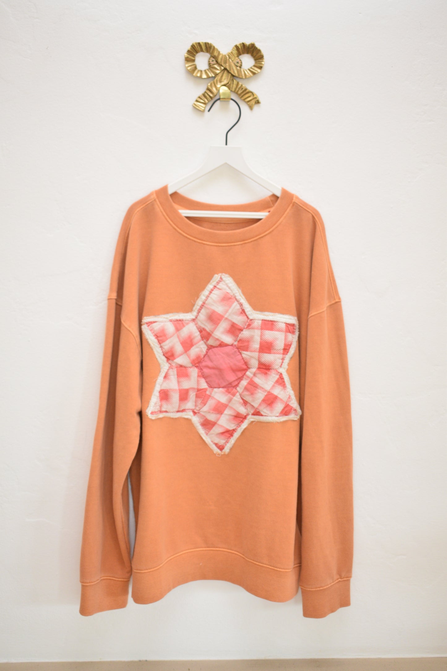 ASA upcycled orange cotton kids sweatshirt with quilted six-pointed star appliqué, size 10–12, on hanger against neutral wall.
