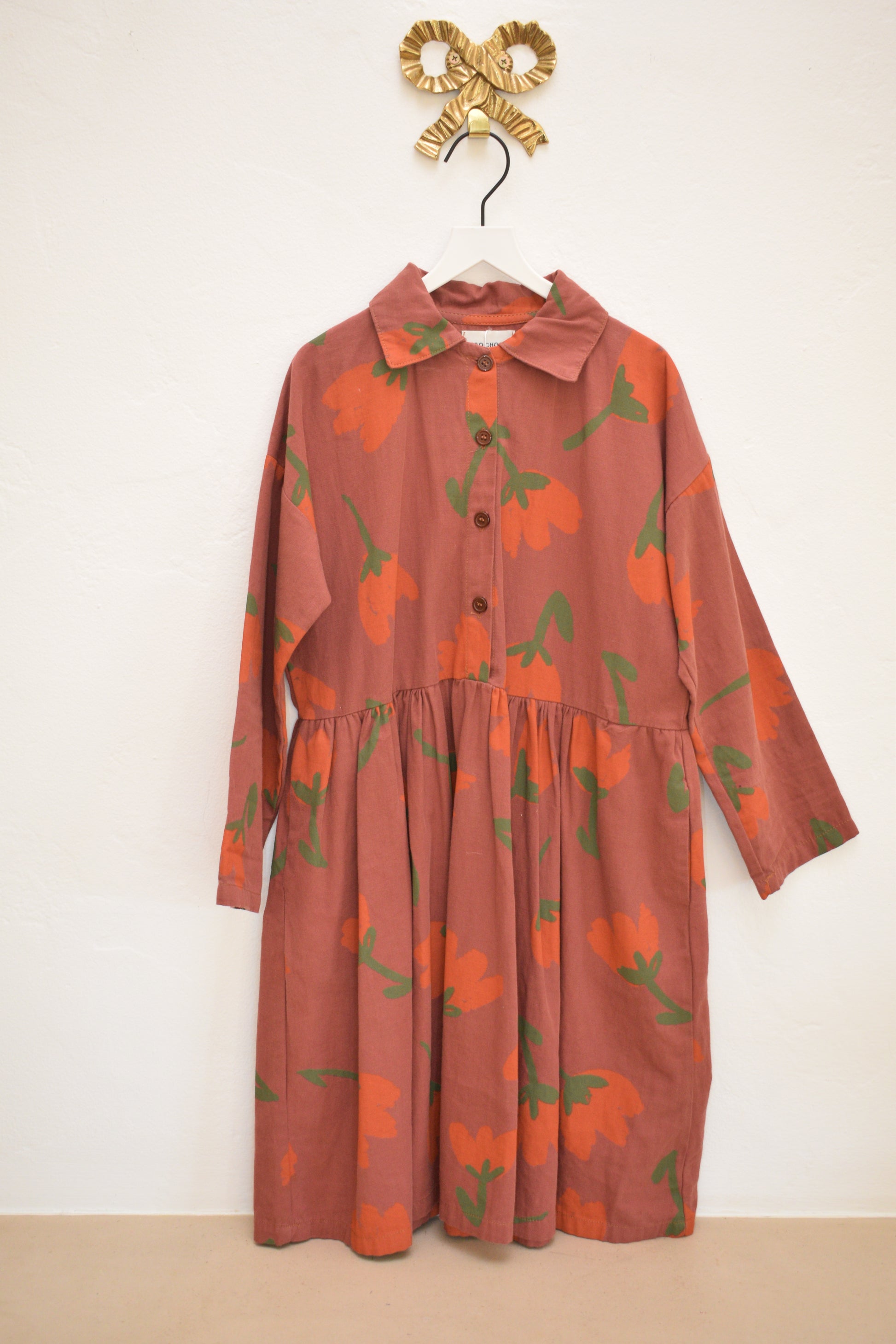 Bobo Choses SS22 ‘I’m a Poet’ clay-red long-sleeve floral shirt dress with gathered waist, size 8–9, on hanger against neutral wall.