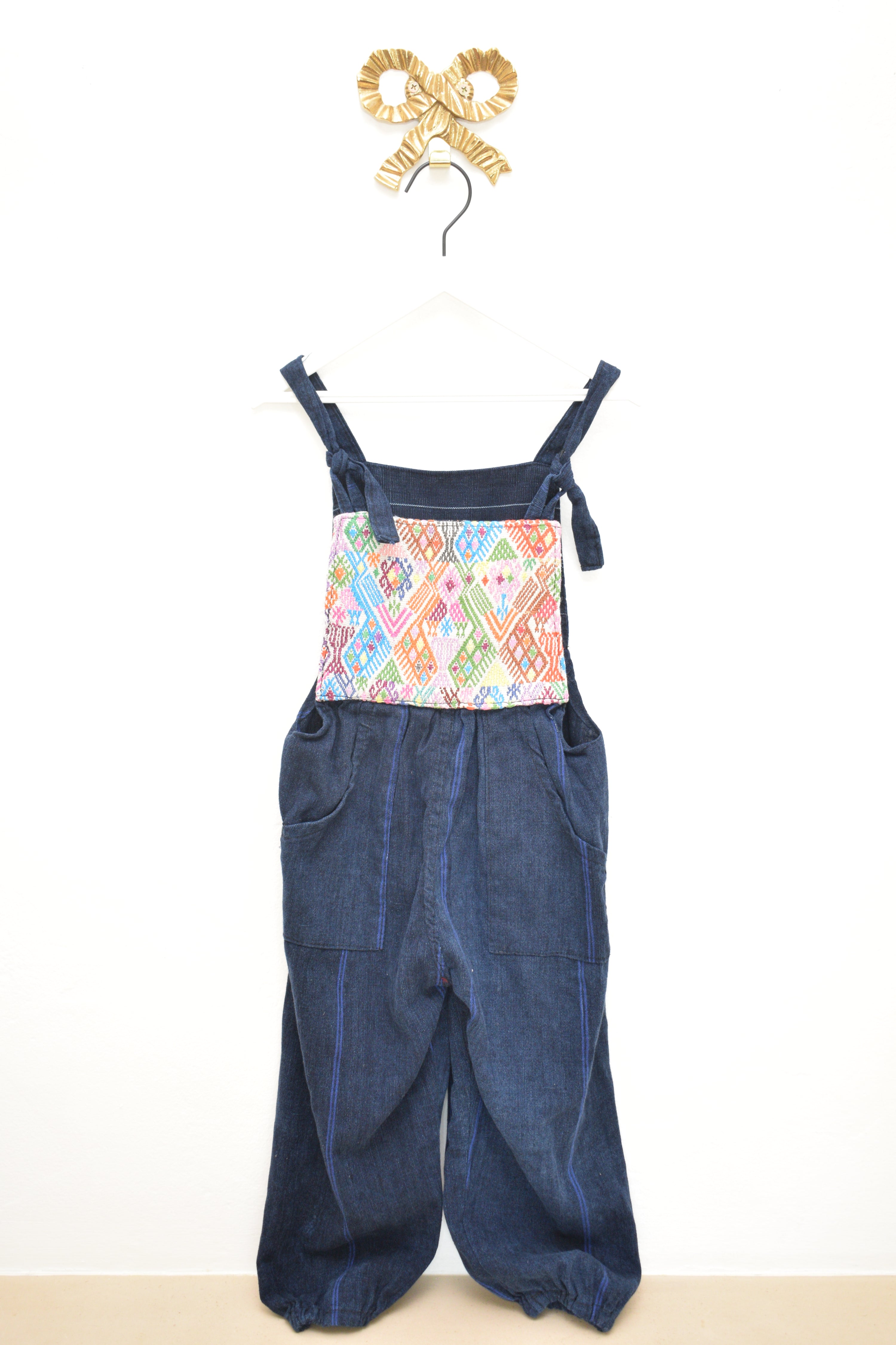 Pair of blue overalls with a colorful patterned pocket on a white background